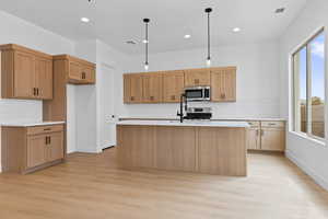 Kitchen with pendant lighting, light wood-type flooring, a center island with sink, and tasteful backsplash
