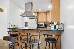 Kitchen with island exhaust hood, a breakfast bar area, dark stone countertops, backsplash, and freestanding refrigerator