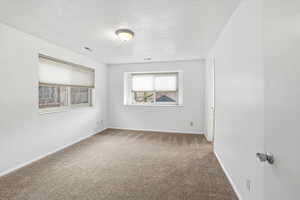 Carpeted empty room featuring a textured ceiling and baseboards