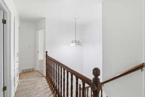 Corridor featuring light carpet, an upstairs landing, and hanging lights