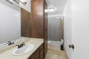 Bathroom with vanity, shower / bath combo with shower curtain, and a textured ceiling