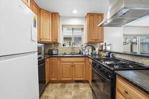 Kitchen featuring black appliances, wood finish cabinets, dark stone countertops, stone finish floors, and recessed lighting