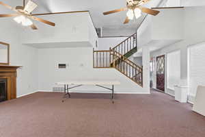 Unfurnished living room featuring a ceiling fan, a high ceiling, carpet floors, and a fireplace