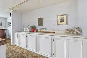 Bar with white cabinets, track lighting, light countertops, white microwave, and light carpet