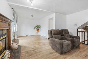 Living room with a textured ceiling, light wood-type flooring, and a tiled fireplace