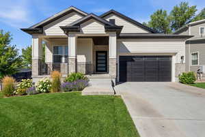 Craftsman house featuring covered porch, an attached garage, a front lawn, concrete driveway, and brick siding