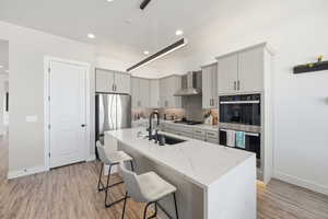 Kitchen featuring stainless steel appliances, a breakfast bar, an island with sink, decorative backsplash, and light stone countertops