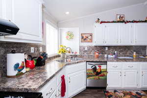 Kitchen featuring backsplash, dark countertops, white cabinets, vaulted ceiling, and ornamental molding