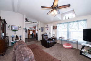 Carpeted living room featuring ceiling fan, vaulted ceiling, and an office area