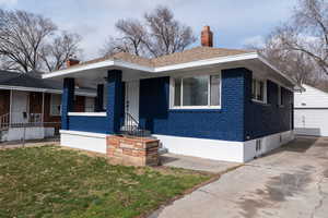View of front of property featuring brick siding, covered porch, an outdoor structure, a chimney, and a detached garage