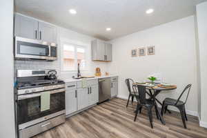 Kitchen featuring stainless steel appliances, gray cabinetry, dark wood-style flooring, backsplash, and a textured ceiling
