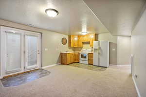 Kitchen featuring a textured ceiling, white appliances, light carpet, and light countertops