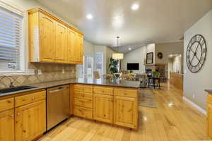 Kitchen featuring dark stone countertops, hanging light fixtures, a peninsula, dishwasher, and decorative backsplash