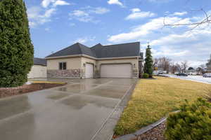 View of home's exterior with stucco siding, stone siding, a garage, driveway, and a yard