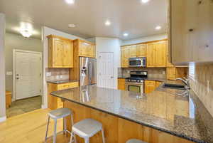 Kitchen featuring dark stone counters, stainless steel appliances, a peninsula, light hardwood floors, and tasteful backsplash