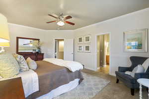 Carpeted primary bedroom with a ceiling fan and ornamental molding