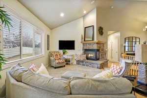 Living room featuring vaulted ceiling, carpet flooring, and a stone fireplace