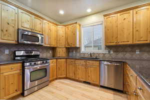 Kitchen with stainless steel appliances, dark stone counters, light hardwood flooring, recessed lighting, and wood finish cabinets