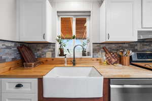 Kitchen featuring white cabinetry, butcher block countertops, stainless steel dishwasher, backsplash, and extractor fan