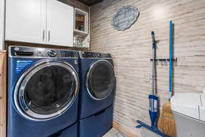 Laundry room with wood walls, separate washer and dryer, and cabinet space