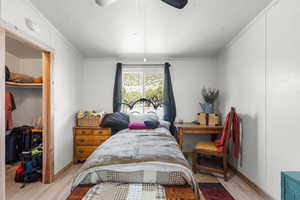 Bedroom with a walk in closet, ornamental molding, wood finished floors, and a ceiling fan