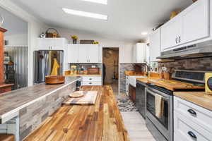 Kitchen with butcher block countertops, stainless steel appliances, white cabinets, vaulted ceiling, and tasteful backsplash