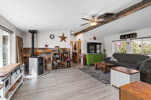 Living area featuring a wood stove, ceiling fan, lofted ceiling with beams, and wood finished floors