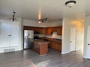 Kitchen featuring stainless steel appliances, wood finish cabinetry, dark wood-type flooring, and a center island