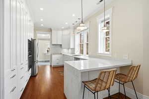 Kitchen with a breakfast bar, a peninsula, light stone counters, white cabinets, and dark wood-style floors