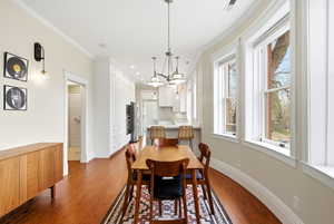 Dining space with light wood finished floors, crown molding, and a chandelier