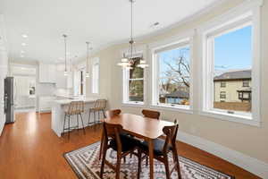 Dining space with ornamental molding, light wood-style flooring, and suspended lighting