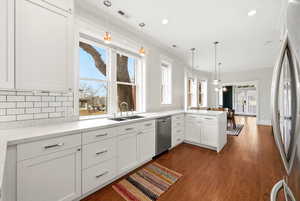 Kitchen with decorative light fixtures, white cabinets, stainless steel appliances, ornamental molding, and dark wood finished floors