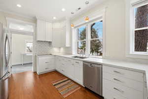 Kitchen featuring white cabinetry, stainless steel appliances, pendant lighting, dark wood-type flooring, and ornamental molding