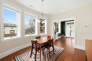 Dining space featuring dark wood-style floors, crown molding, and suspended lighting