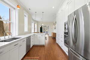 Kitchen with stainless steel appliances, white cabinets, ornamental molding, hanging light fixtures, and dark wood finished floors