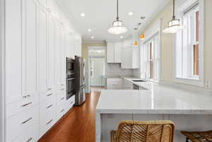 Kitchen with a breakfast bar, white cabinets, light stone counters, crown molding, and a peninsula