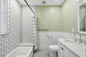 Full bathroom featuring vanity, a wainscoted wall, and shower / bathtub combination with curtain