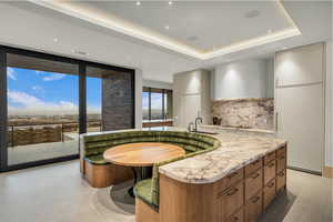 Kitchen with modern cabinets, expansive windows, a kitchen island with sink, light stone countertops, and tasteful backsplash