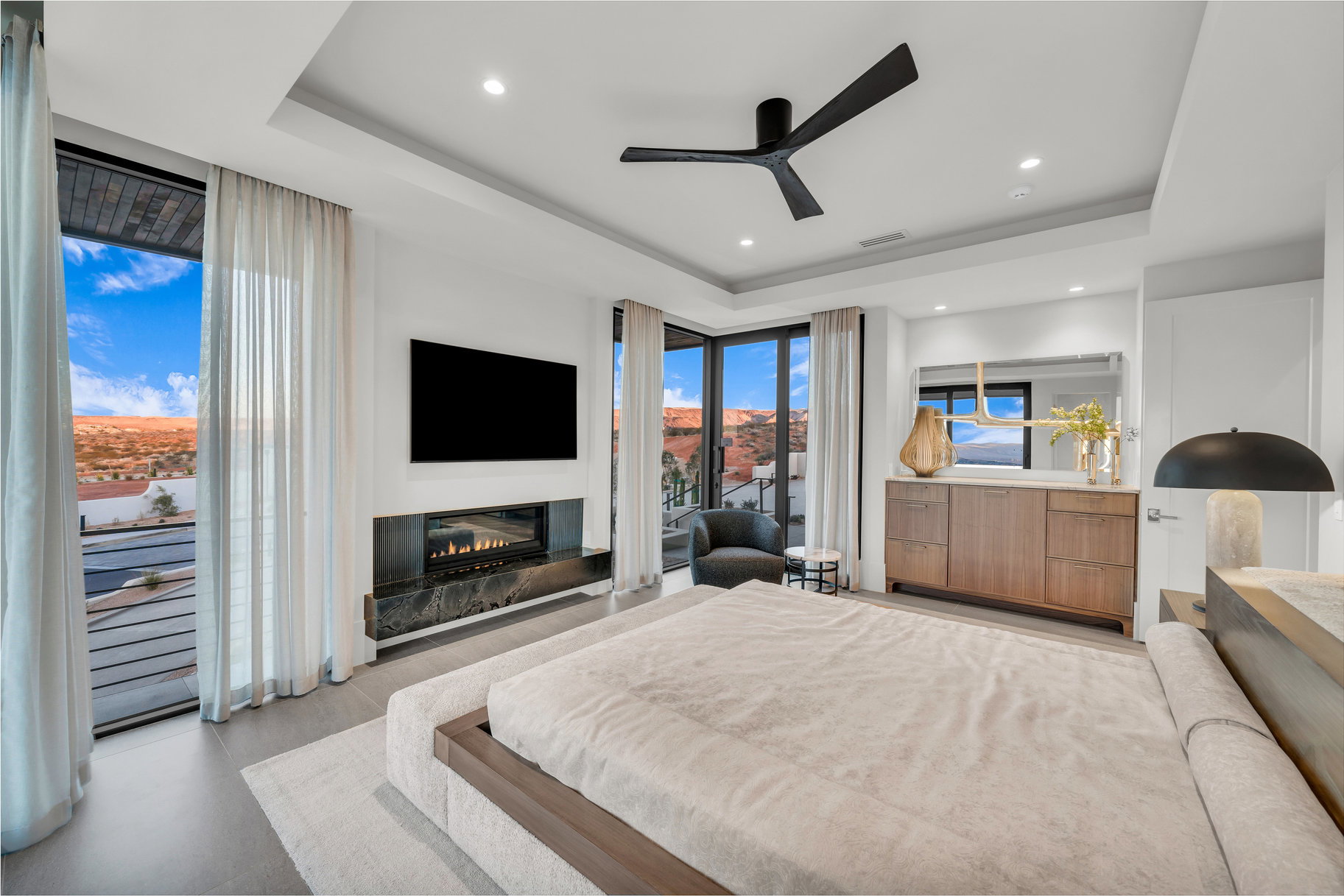 Bedroom with access to outside, a tray ceiling, a ceiling fan, a glass covered fireplace, and recessed lighting