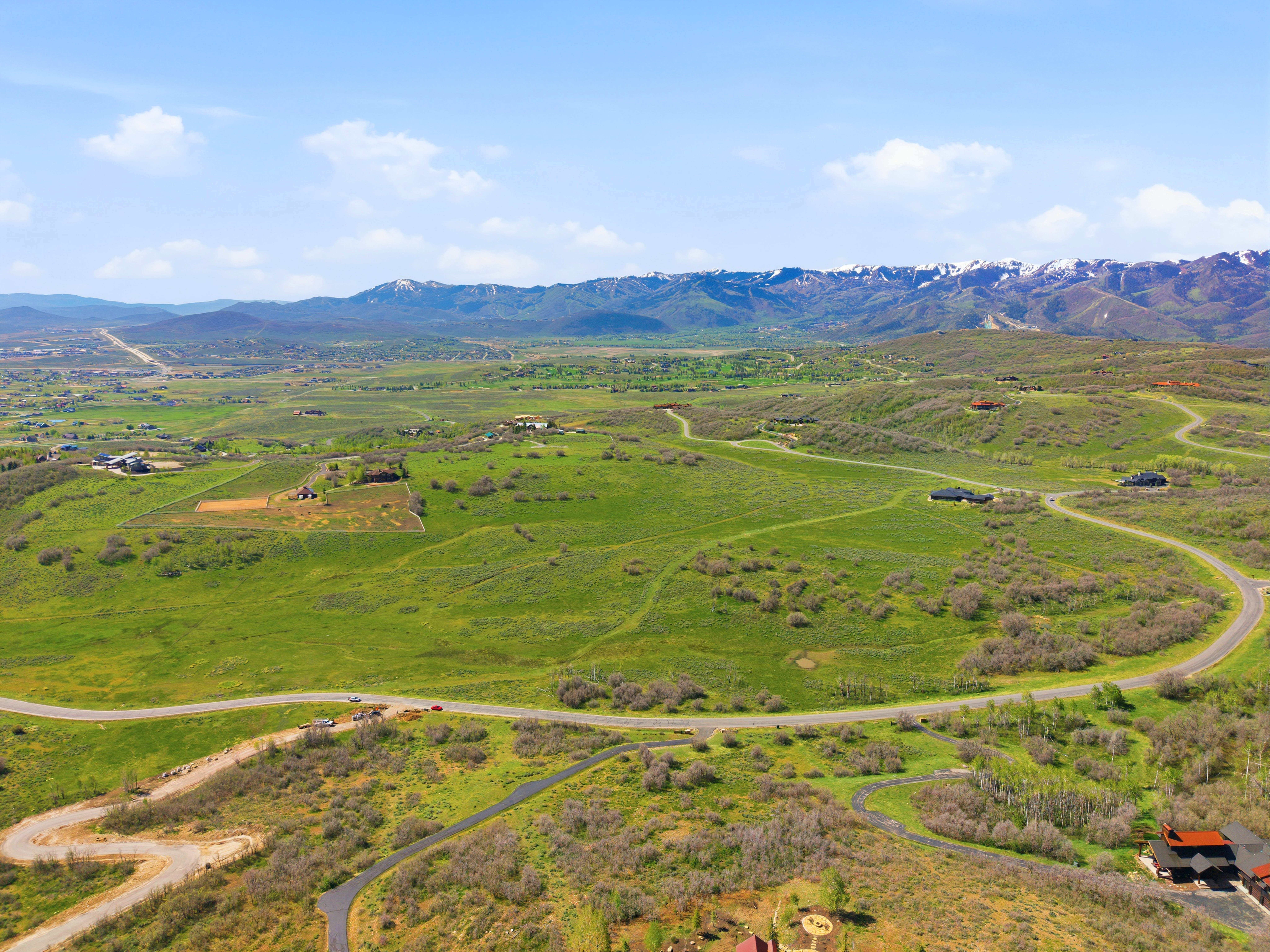 Expansive green landscape featuring winding roads and distant snow-capped mountains under a clear sky
