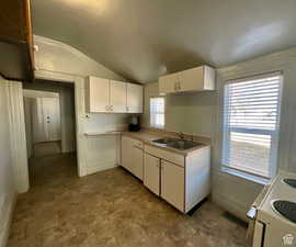 Kitchen featuring lofted ceiling, white cabinets, light countertops, electric range, and stone finish flooring