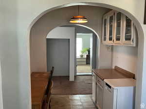 Kitchen with glass fronted cabinets, light colored carpet, white cabinetry, white dishwasher, and arched walkways