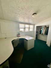 Home office featuring a textured ceiling, dark colored carpet, and built in study area
