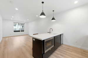 Kitchen with a peninsula, light wood-style floors, stainless steel appliances, hanging light fixtures, and light stone countertops
