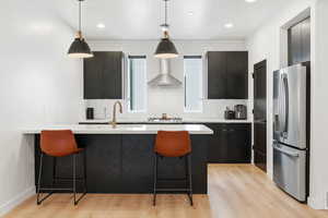 Kitchen featuring dark cabinetry, a breakfast bar, decorative light fixtures, and stainless steel fridge with ice dispenser