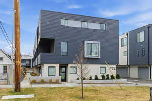 Contemporary house featuring a front yard, stucco siding, a balcony, and a garage