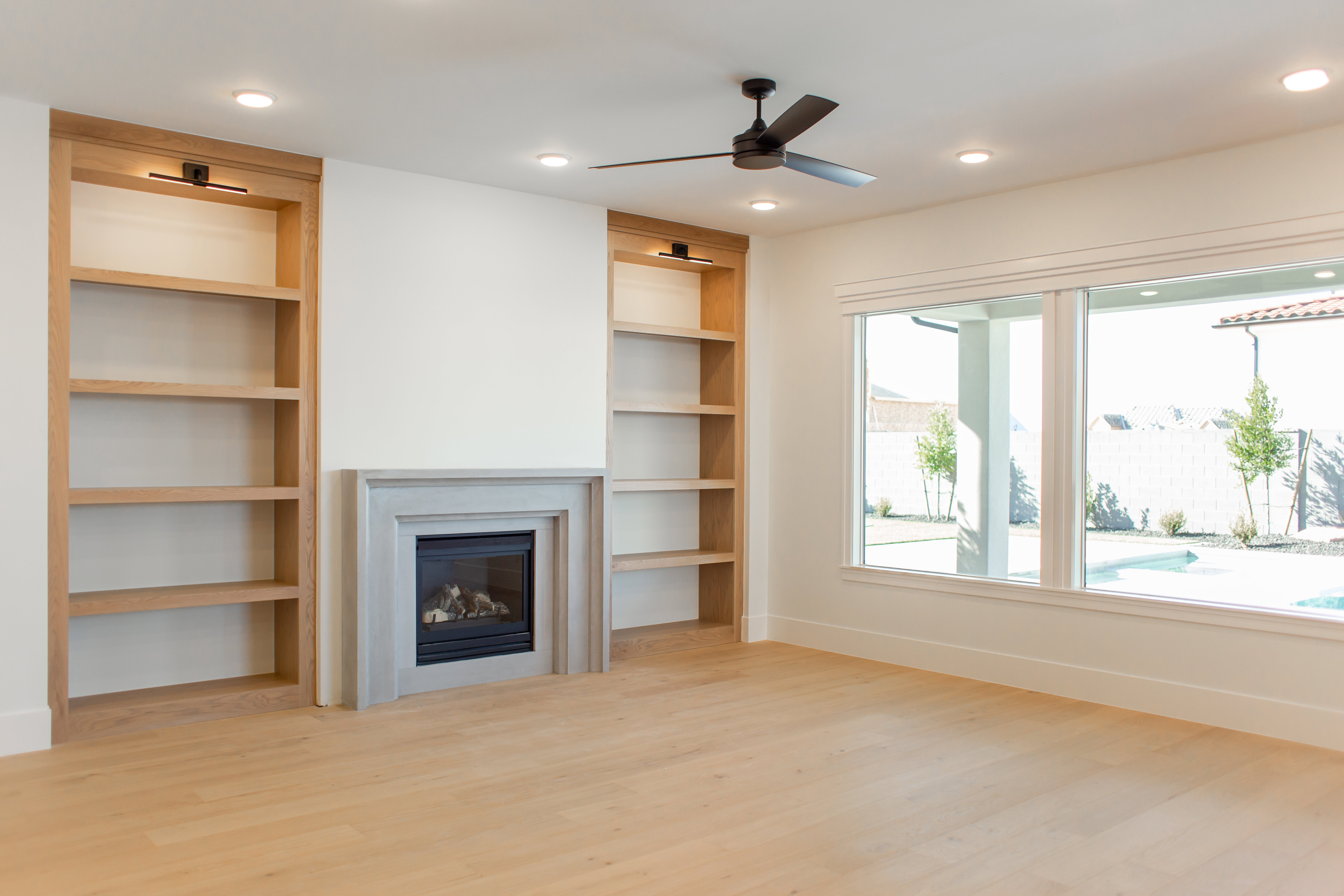 Unfurnished living room featuring light wood-style flooring, built in features, ceiling fan, a glass covered fireplace, and recessed lighting