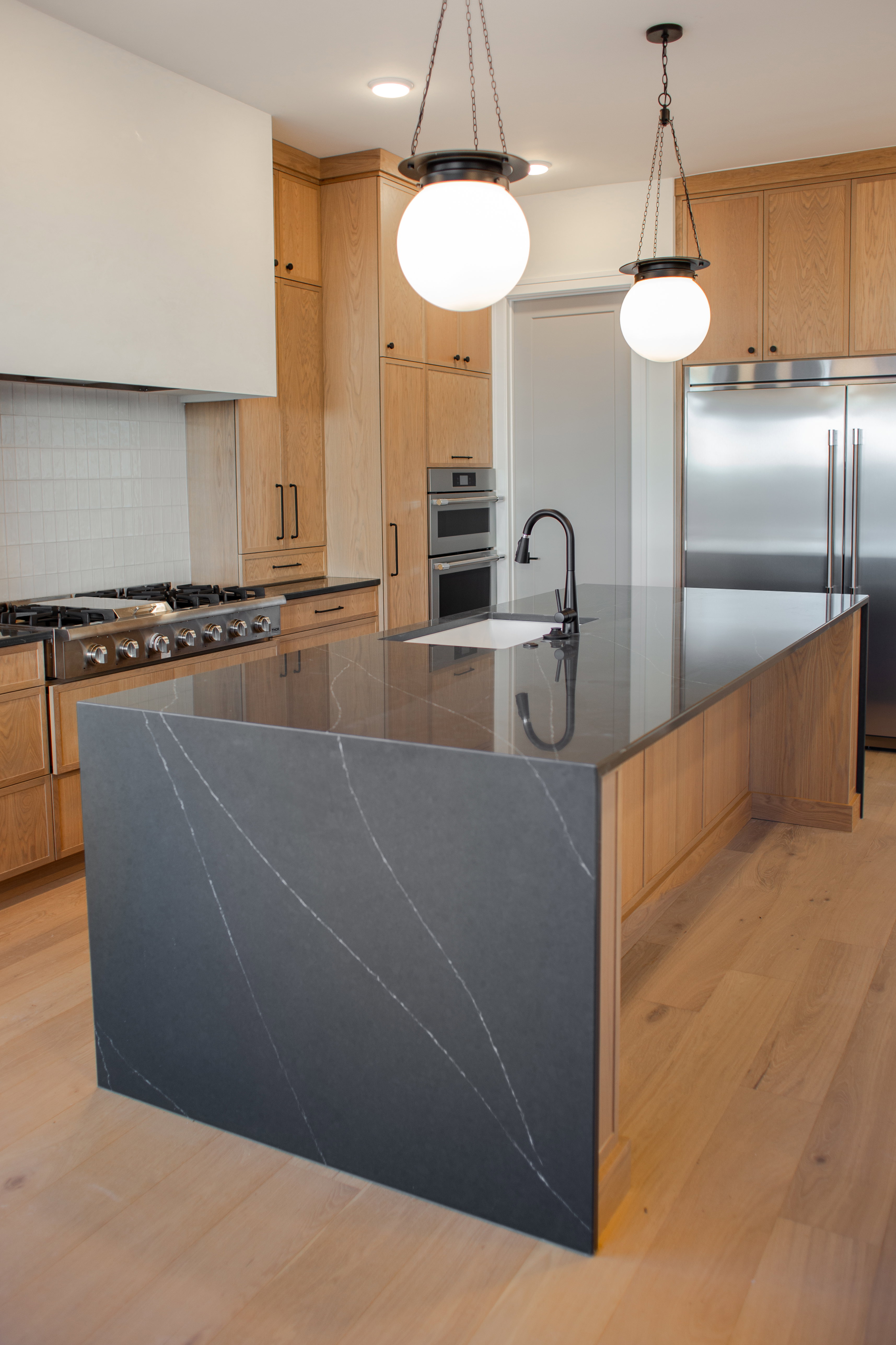 Kitchen featuring dark stone countertops, decorative light fixtures, stainless steel appliances, light wood-style floors, and a large island