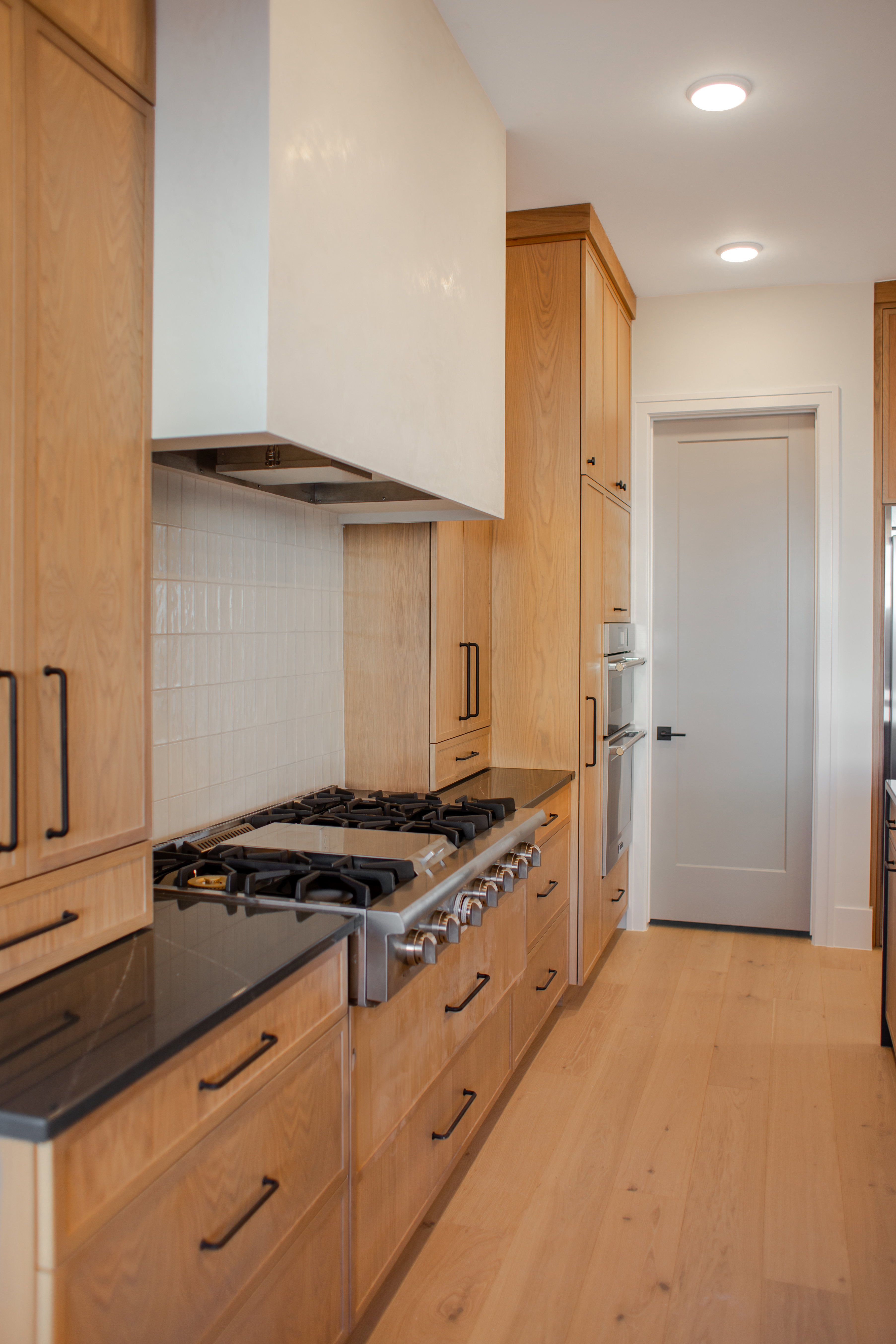 Kitchen featuring light wood-type flooring, stainless steel appliances, dark stone countertops, decorative backsplash, and recessed lighting
