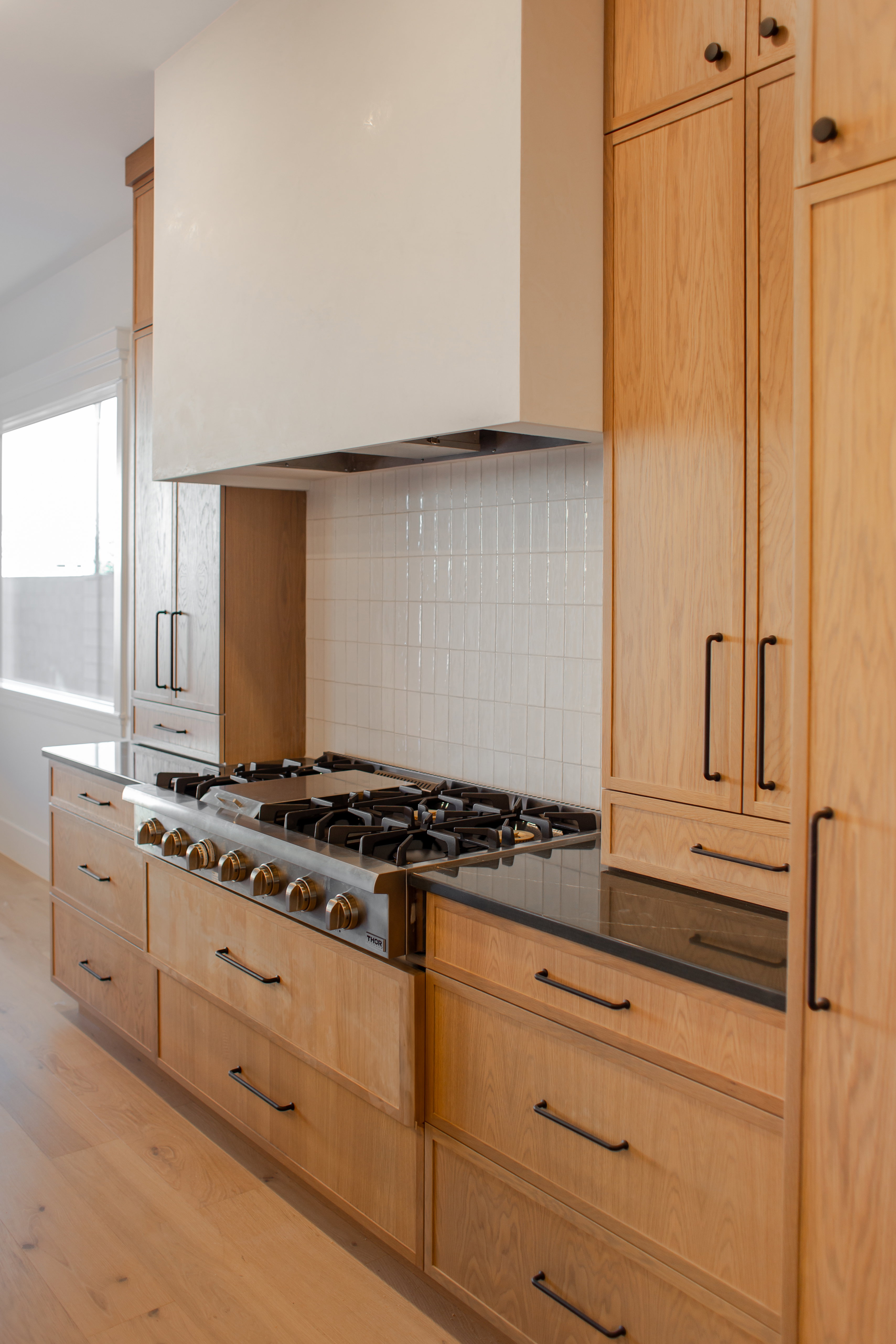 Kitchen featuring light wood finish cabinets, stainless steel gas stovetop, light wood finished floors, dark stone countertops, and tasteful backsplash